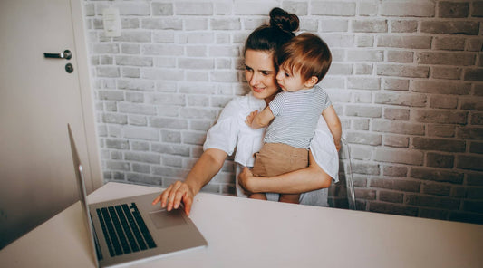 Mother balancing work and childcare, carrying baby while using computer.