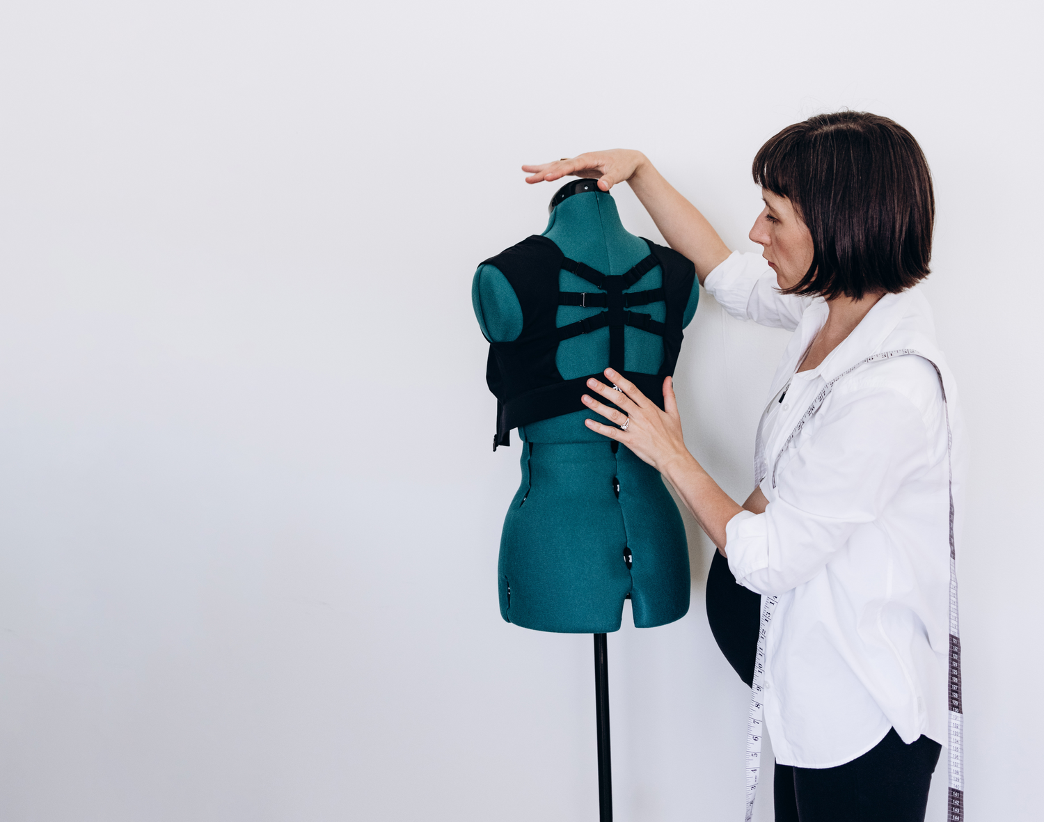 Designer adjusting a black Etalon posture bra on a mannequin during a fitting session.