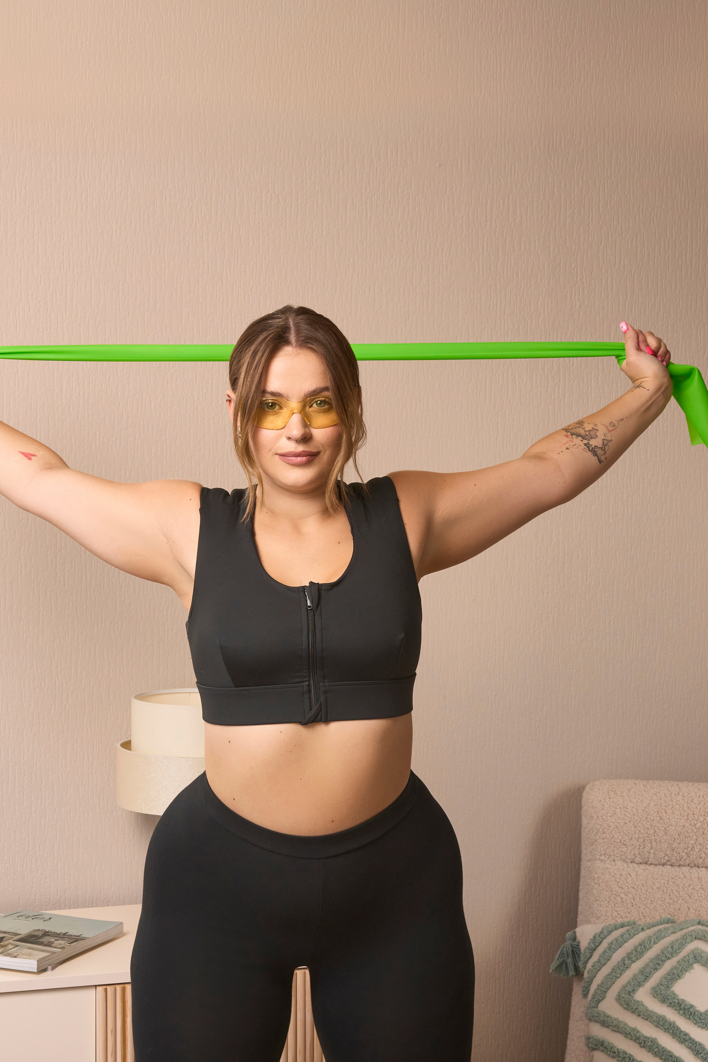 A woman in a black Etalon bra uses a green body posture band for a side stretch to relieve tension.