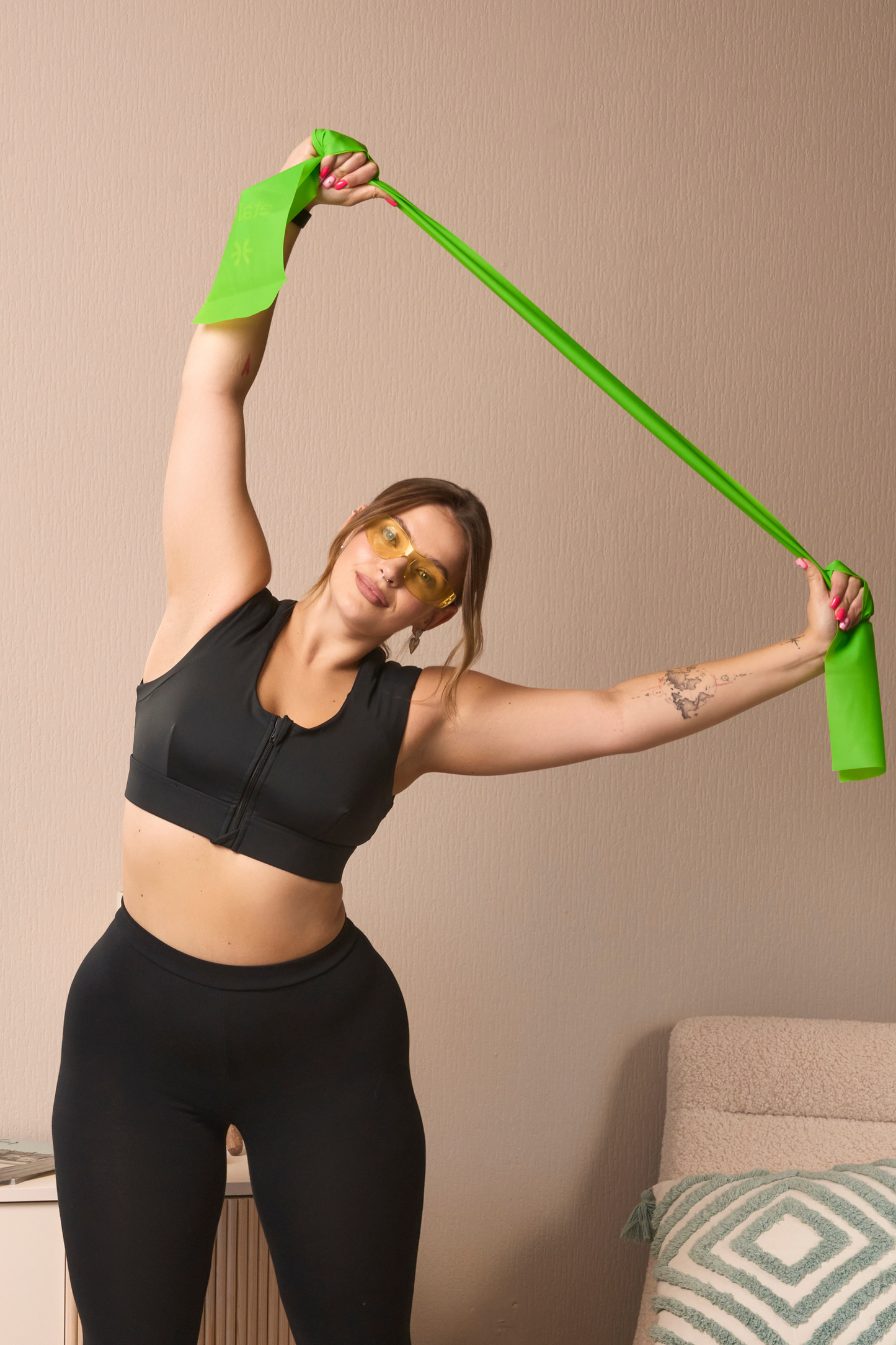A woman in the Etalon posture bra performs a shoulder stretch with a green workout band.