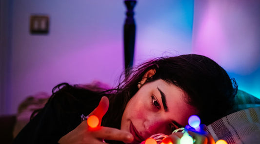 Woman resting in bed, holding holiday lights while feeling down.